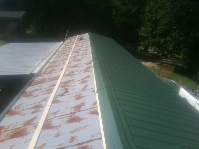 Old rusted panels beside newly installed green metal roofing — Wind Damage Roof Repair by Roofing Brothers in Aynor