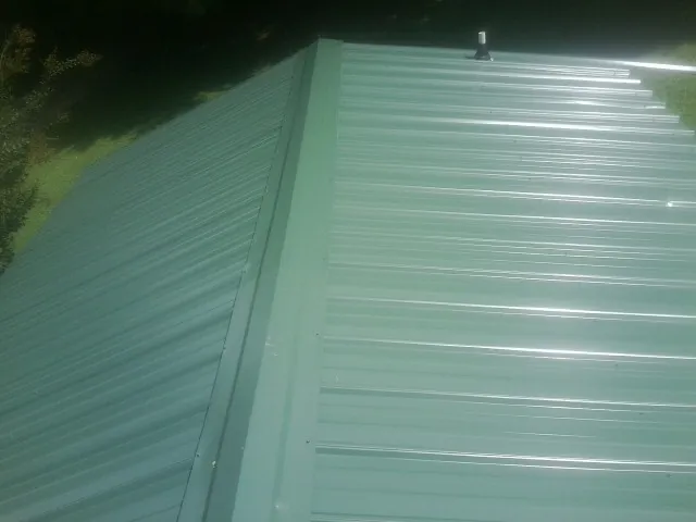 New green metal panels meeting at the ridge of a roof — Flat Roof Repair work by our crew in Aynor