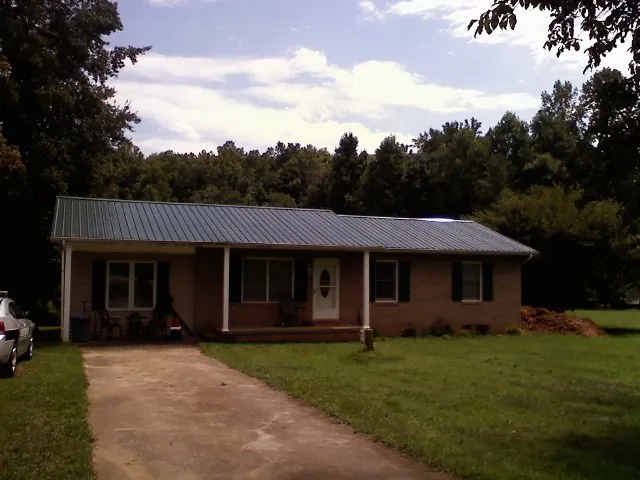 Dark green metal roof on a brick ranch with a covered porch in Aynor
