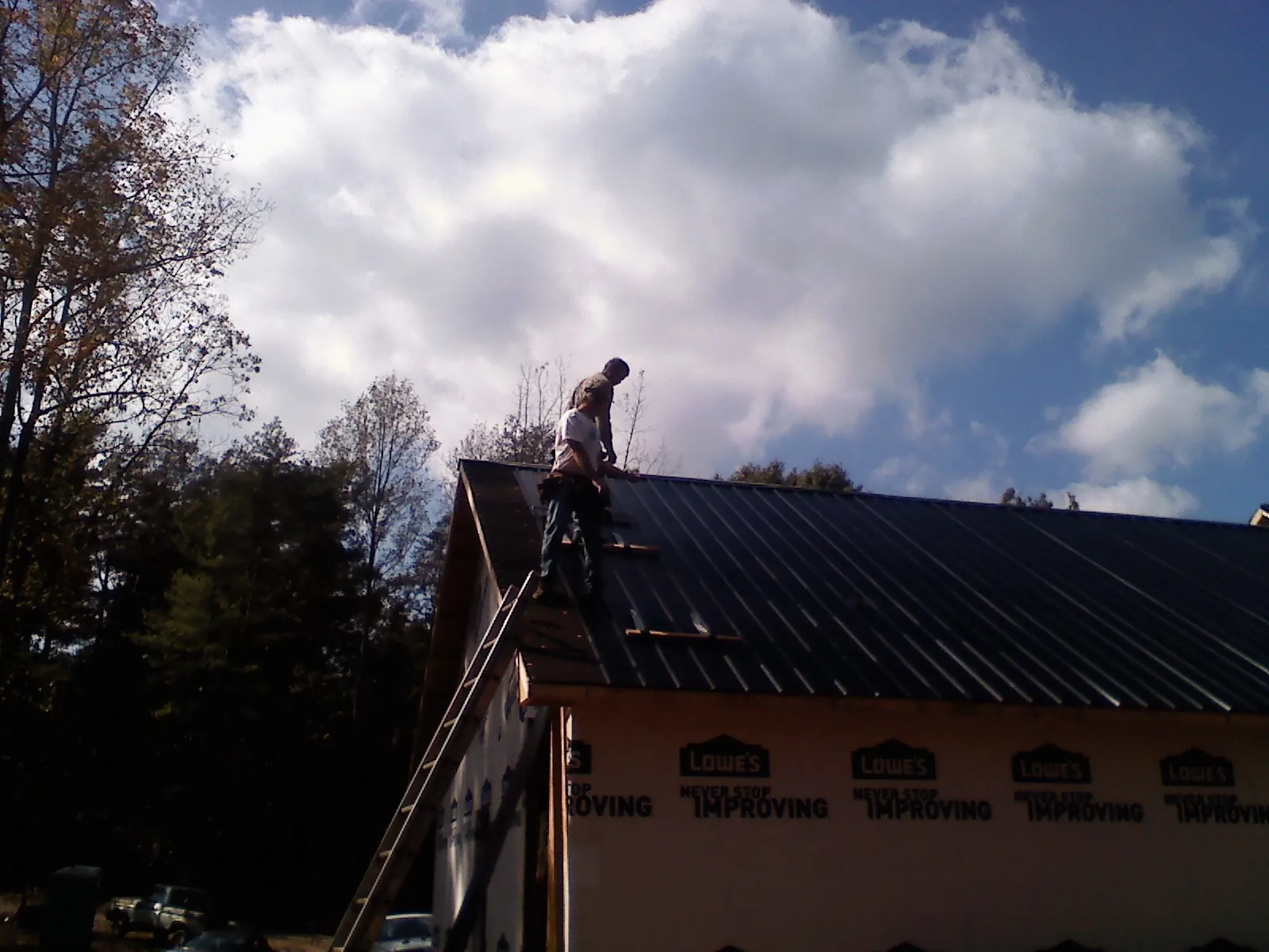 Roofer fastening dark metal panels high against a cloudy sky, from a Roof Inspection job in Aynor