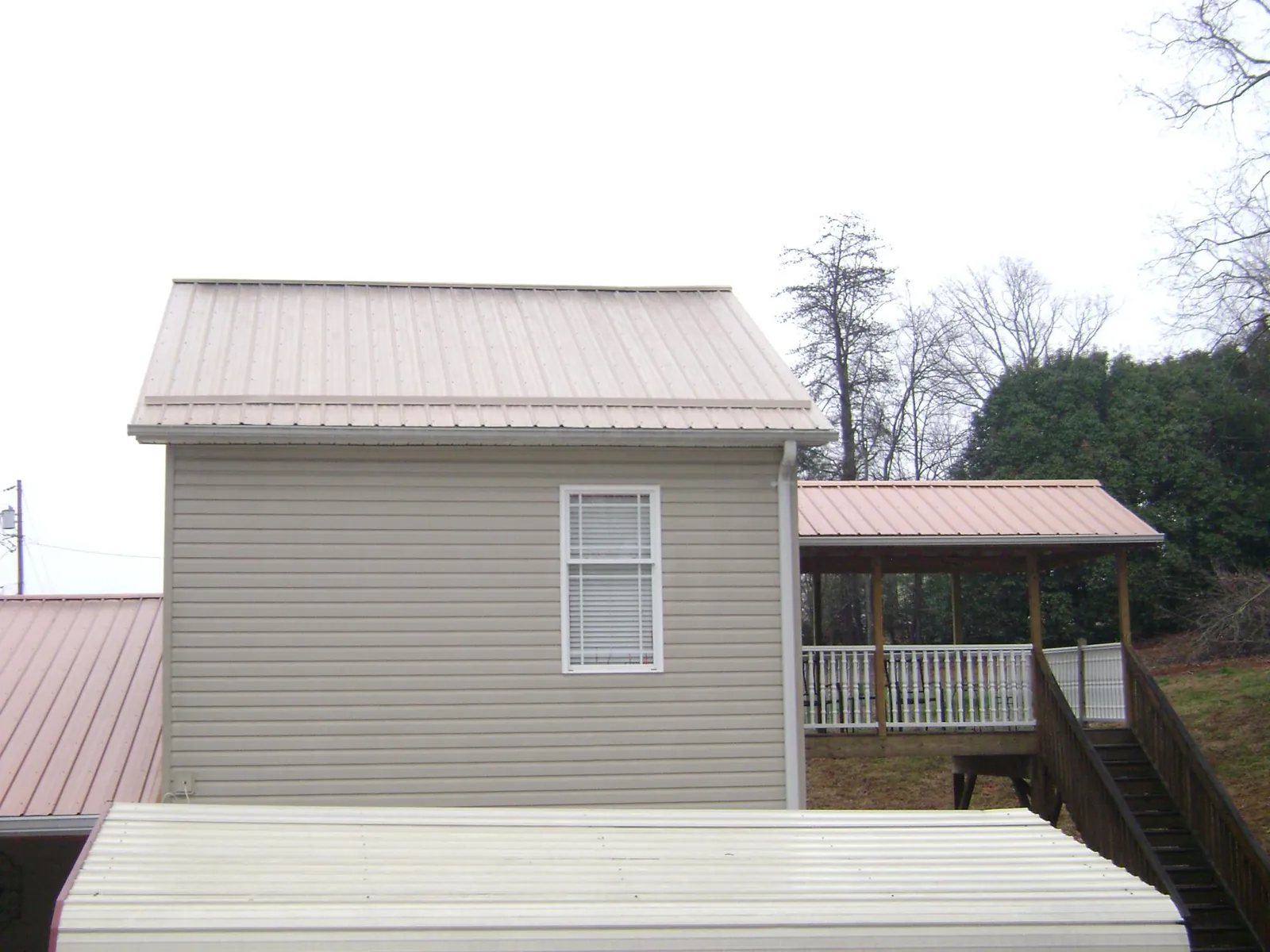 Tan metal roofs on a two story addition and attached porch, from a Roof Replacement job in Aynor